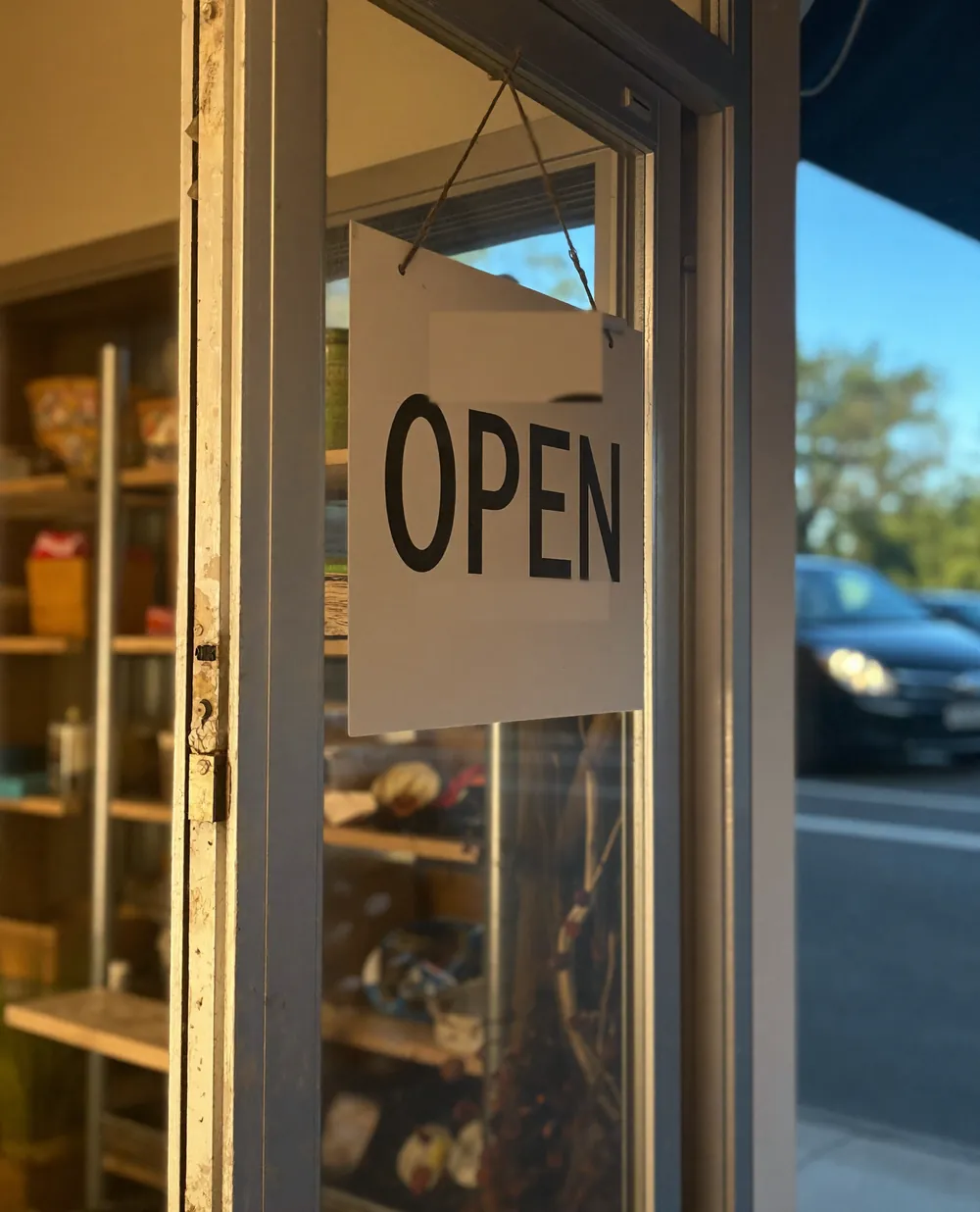 A shop door at opening time with an open sign hanging in the glass and the shelves lit inside
